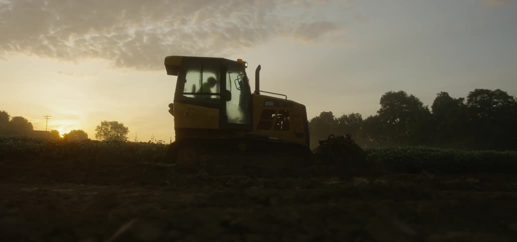 A tractor travels in a field under a cloudy sky