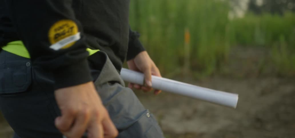 A man carrying a thermos and a rolled paper walks into a forest