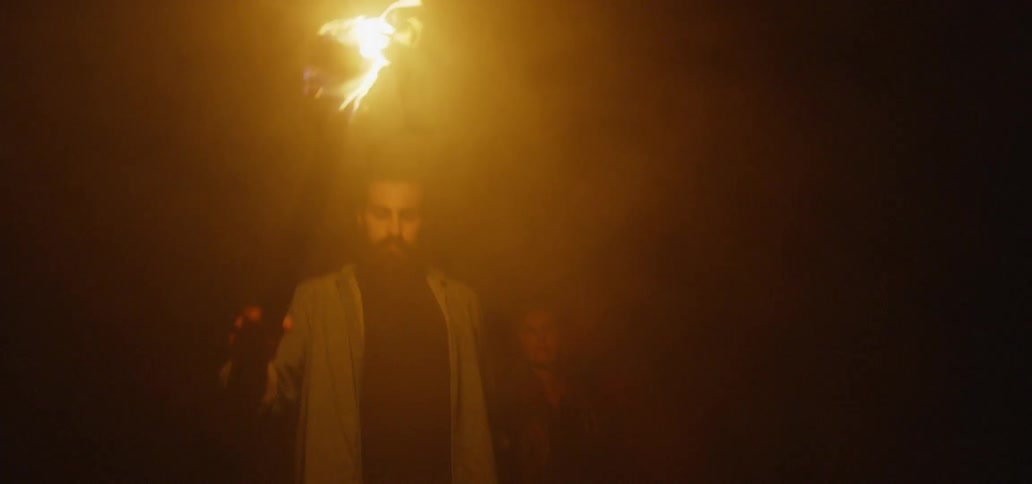 Bearded man holding the hand of a woman and a torch while walking at a dark place