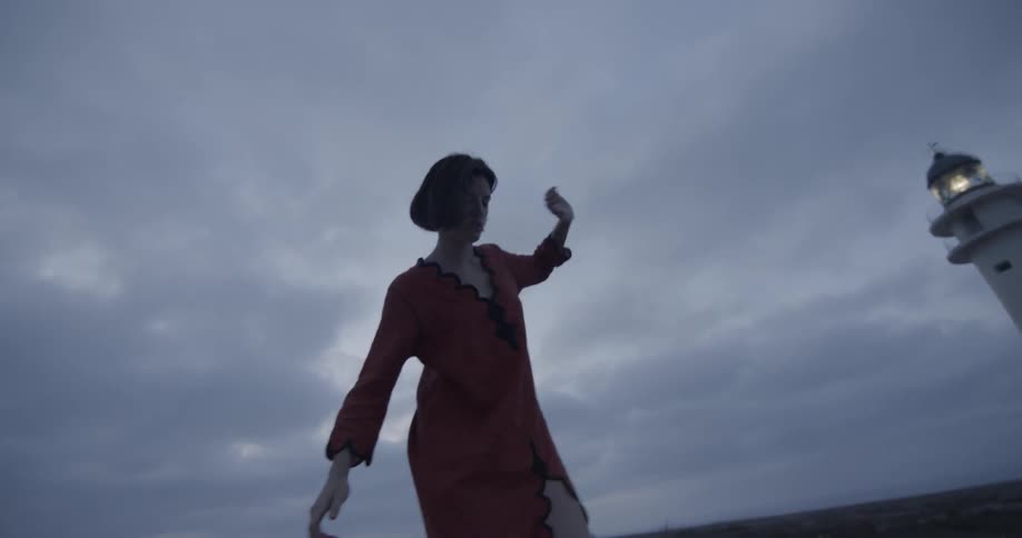 A girl balances on something in front of a lighthouse