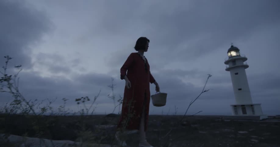 A girl balances on a path of sand in front of a lighthouse