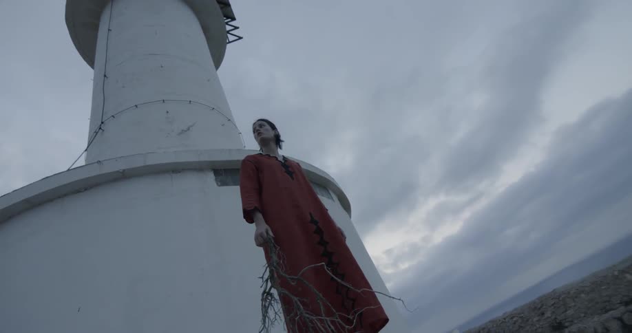 Woman in red dress holds branch near lighthouse