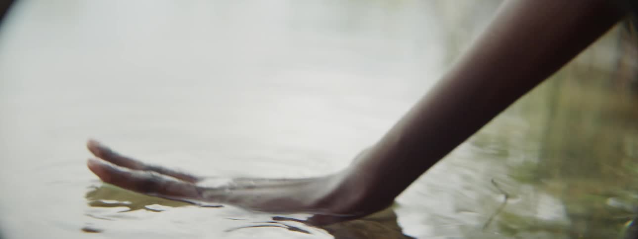 A person scoops water from the pond