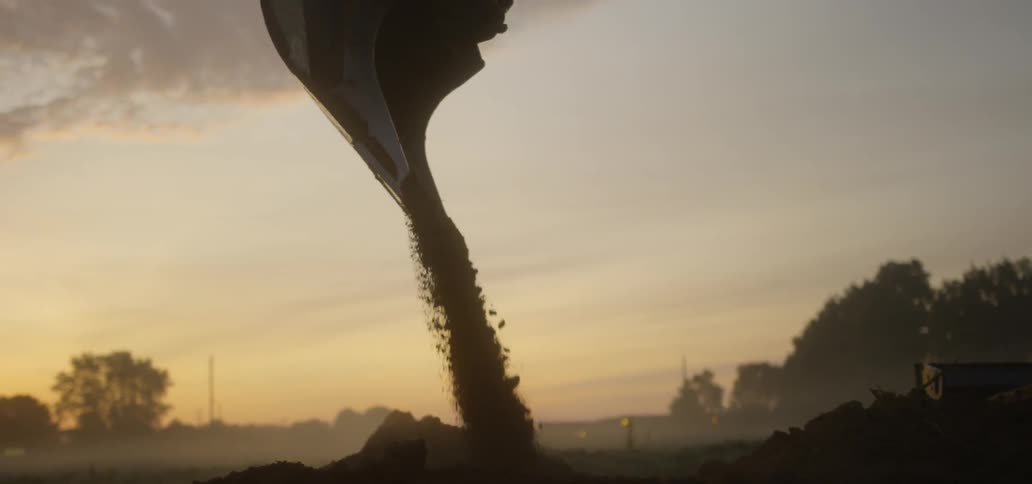 Crane drops dirt on ground at sunset