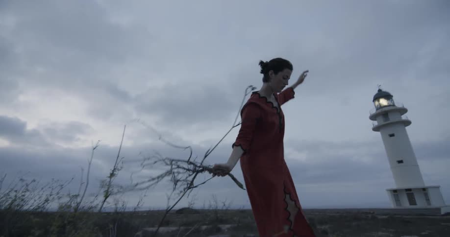 A woman holds a dry tree branch as she balances on a stone wall
