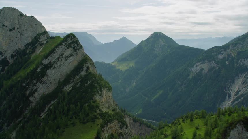 Mountain range has green grass and trees growing in places