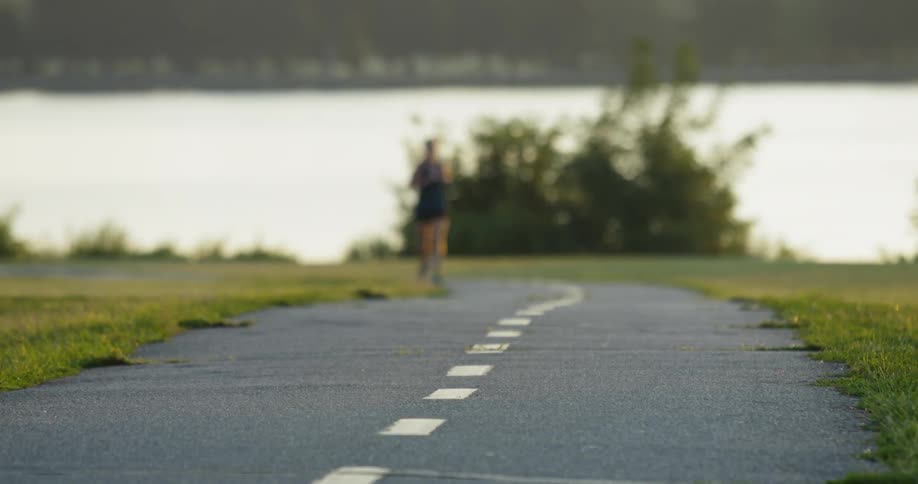 A runner runs down a track with a lake behind her