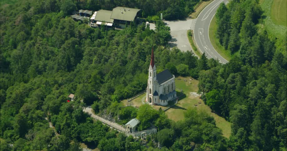 Tall church with a red steeple at the top of a hill of trees and houses