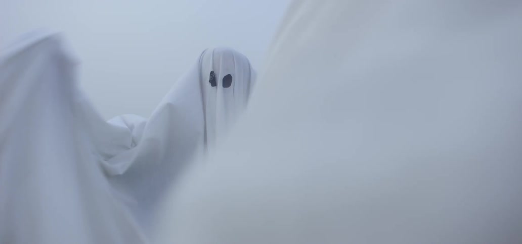 Person wearing a white sheet ghost costume waving their hands