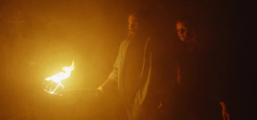 Man holds torch while navigating with girlfriend through a forest
