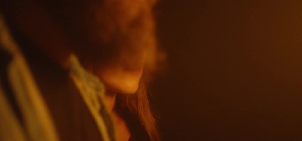 A bearded man and a woman are illuminated by firelight