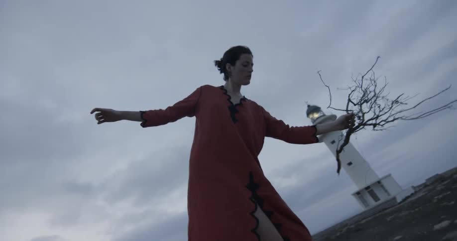 Woman in pink dresses walks precariously near lighthouse