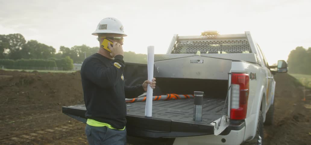 Man in a hard hat stands at the back of a pickup talking on the phone