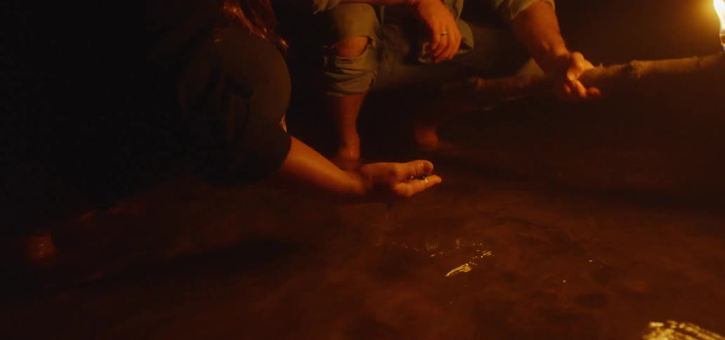 Man and women sit near shallow water with man holding torch