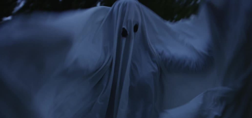 A person dressed as a ghost outside is running around swinging their arms