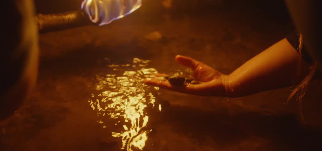 A person searches in the water as another holds a torch for light