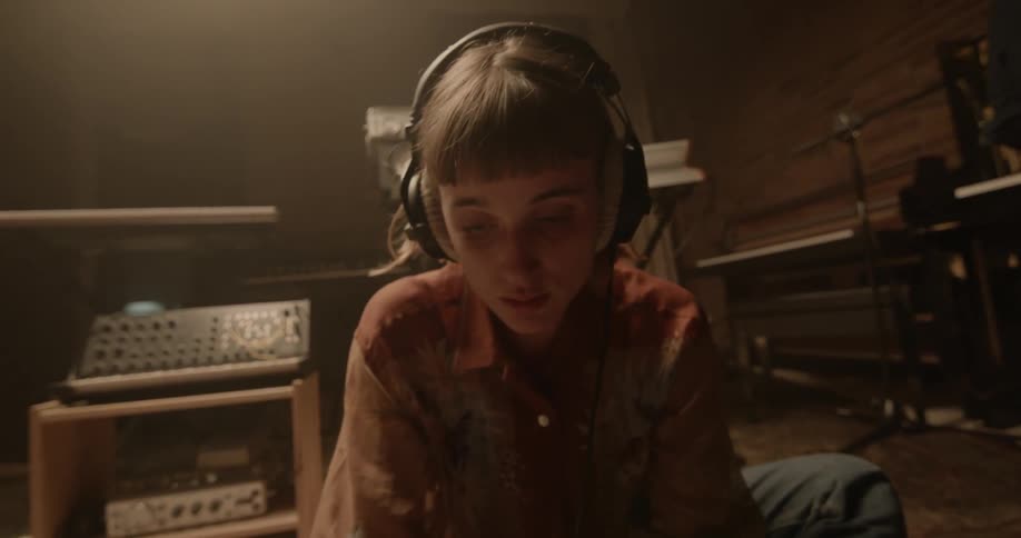 A woman sits on the floor wearing headphones in front of a mixing board