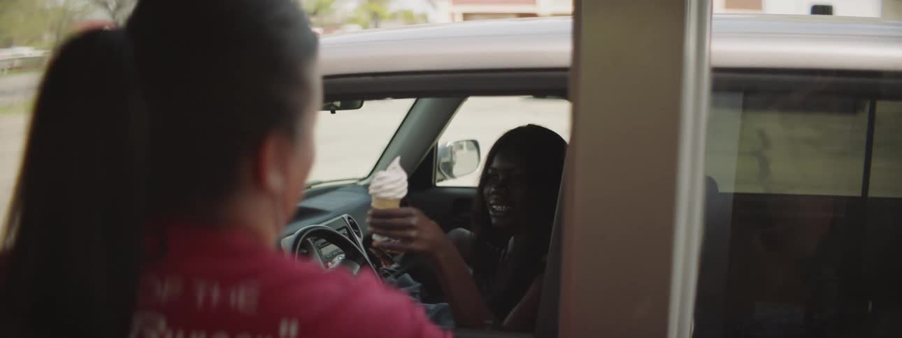 A woman collects food and an ice cream from a drive through