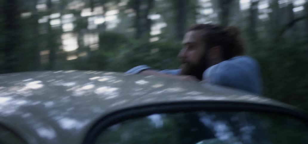 A woman and man lean on the vehicle talking in the woods