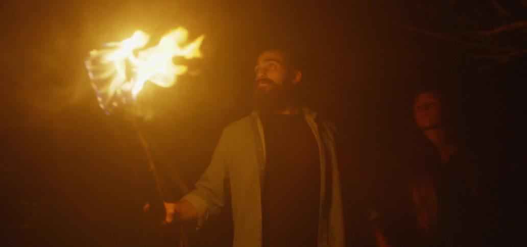 Couple Walking Through Woods Carrying A Torch