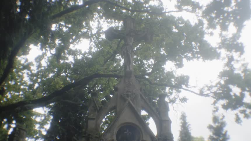 A cross sits on top of a chapel under trees
