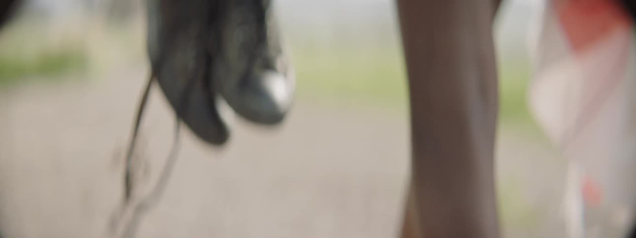 A person is walking and carrying a pair of shoes in their hand