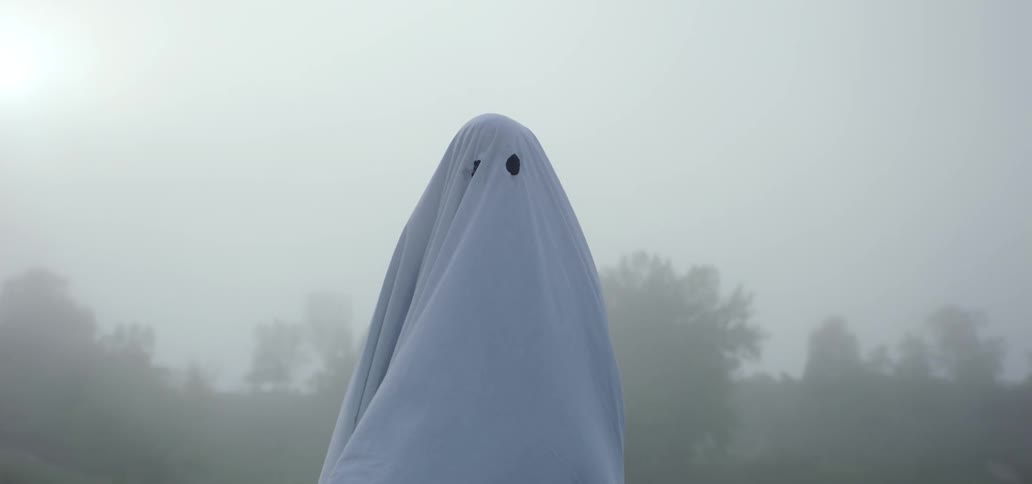 A person is dressed as a ghost with a white sheet on their head