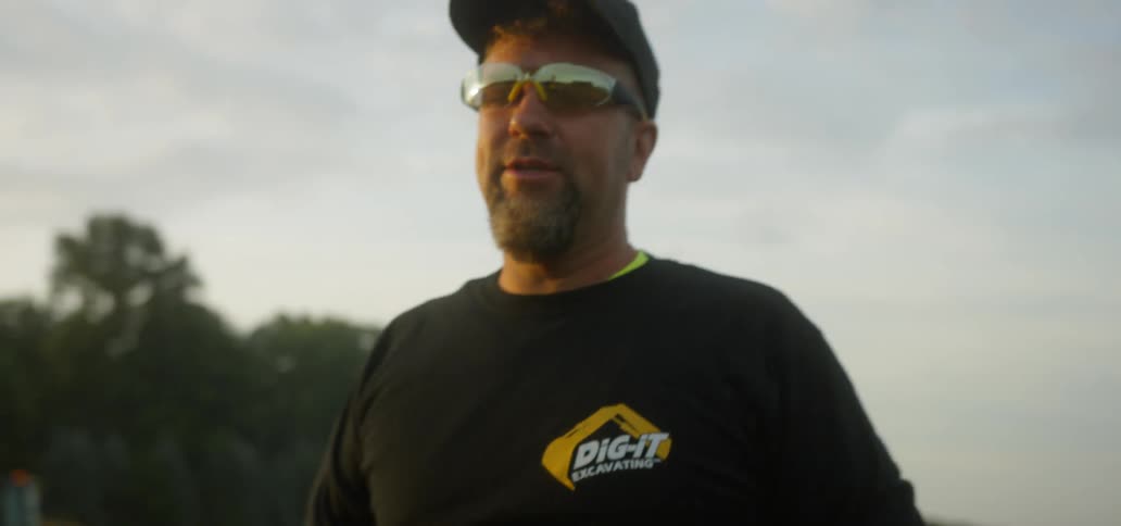 Man in hat gestures towards field with construction equipment in it