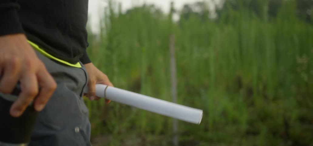 A man walks in the grass carrying blueprints
