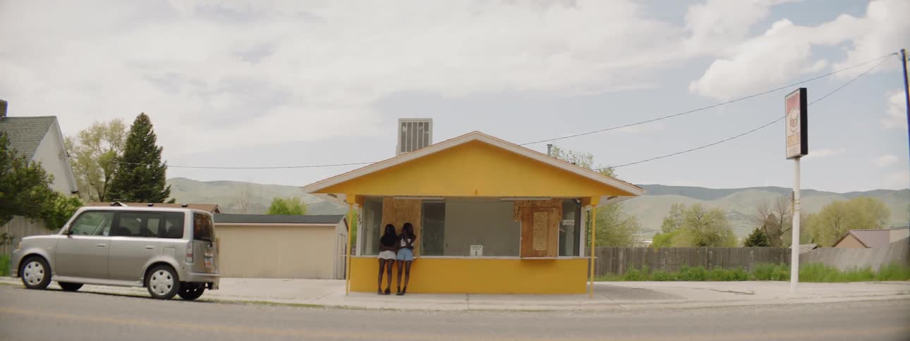 Two women stand at a boarded up house as cars go by on the road