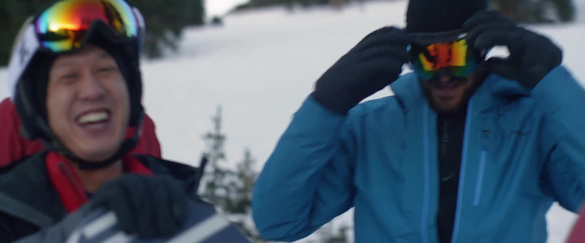 Young men are smiling and laughing on a snowy mountain while wearing skiing gear