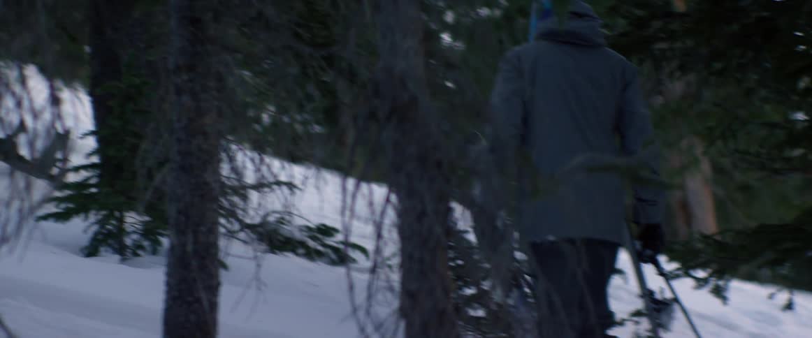 A man trudges up a snowy hill carrying ski gear