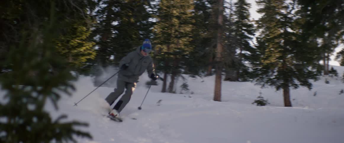 Someone skiing downhill in a wooded area on a sunny day