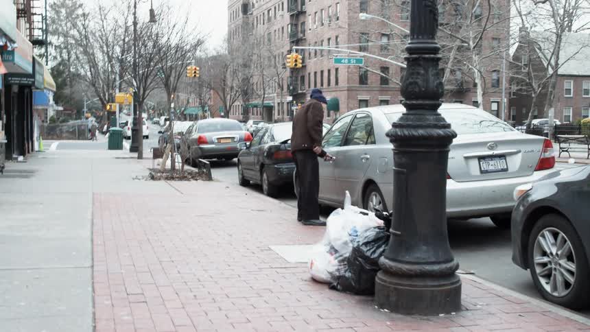 A man approaches a car parked on a city street, opens its door, and gets in