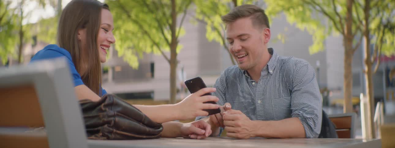 A man looks at a phone a woman is holding out as they both laugh
