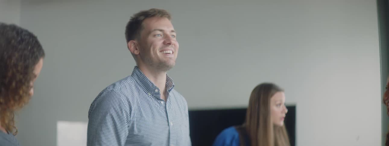 Man and woman are smiling and talking to other people in room