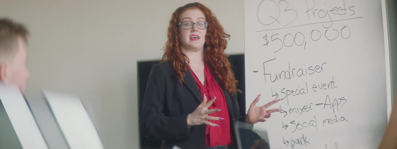 Woman stands in front of a whiteboard talking and gesturing