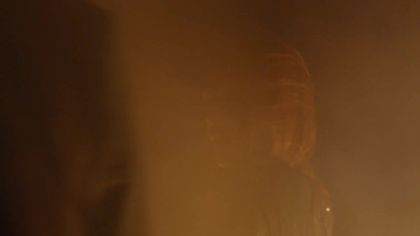 A man and a woman standing in the dark with smoke blowing past them