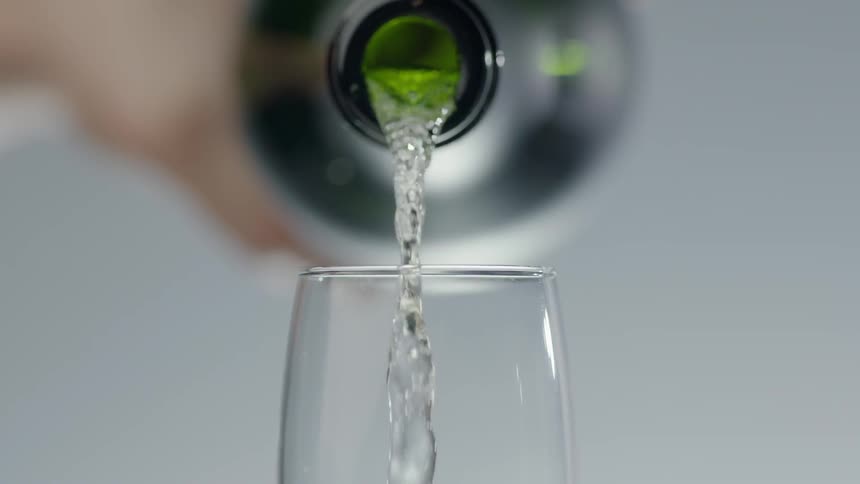Liquid pours out of a green bottle into a champagne glass