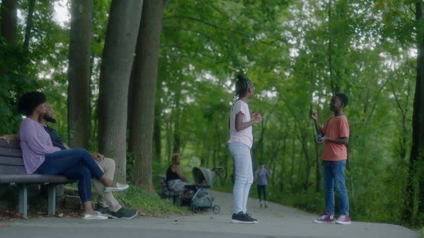 A couple sitting on a park bench watching teens in front of them blow bubbles