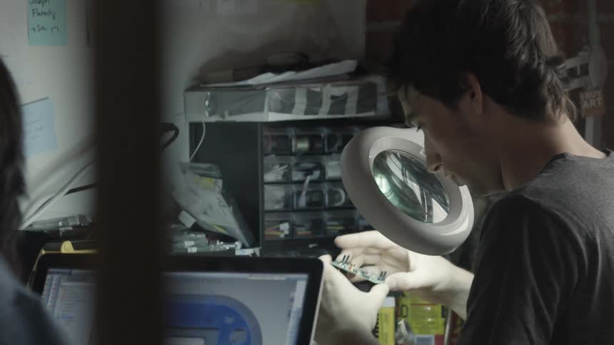 Man looks through a magnifying glass at electronics