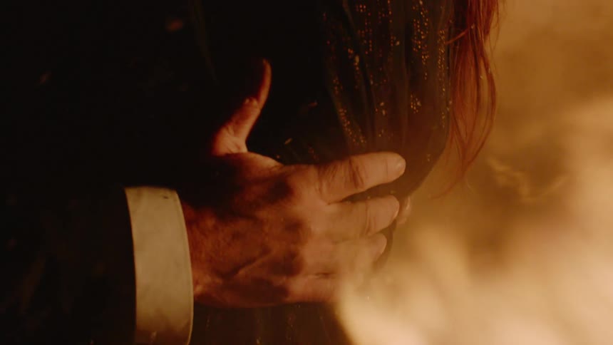 A man and woman holding each other with fire burning behind them