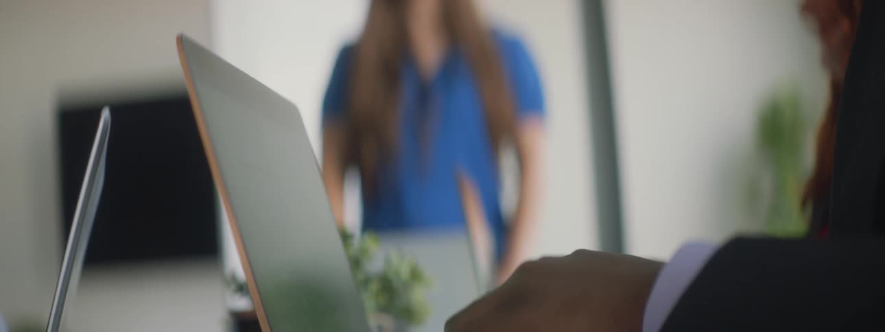 Person uses laptop while woman talks in background