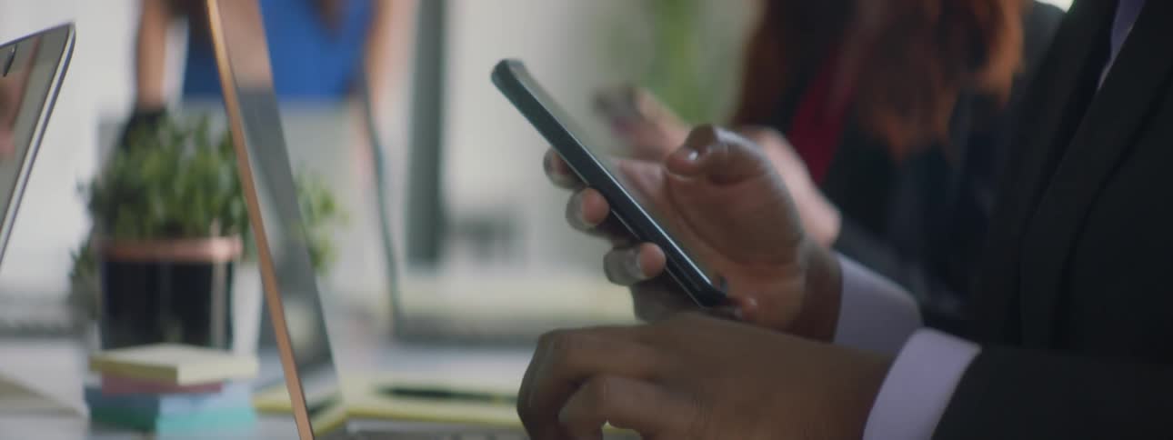 People sit at a table looking at phones and typing on laptops