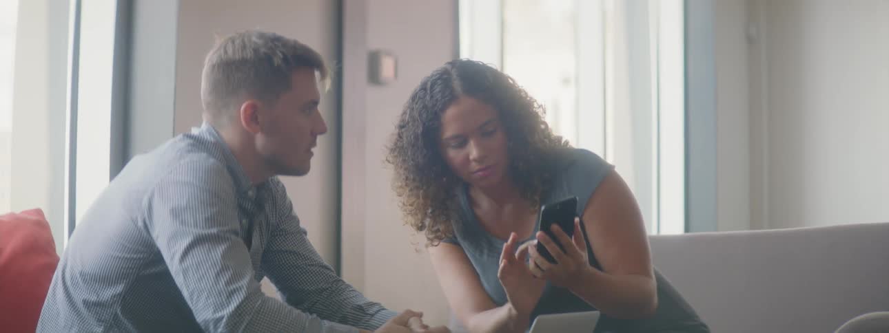 A man and woman talk while looking at her phone