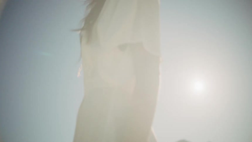 A woman in a white dress walks in a desert on a sunny day