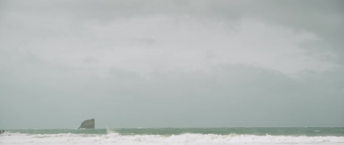 Ocean waves crashing in the ocean with a large rock in the background