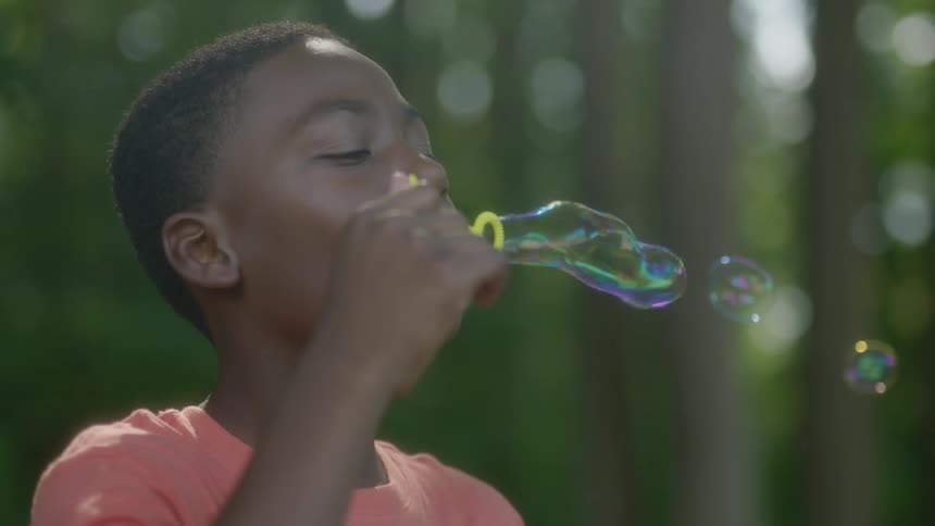 A young boy blows bubbles with a yellow wand