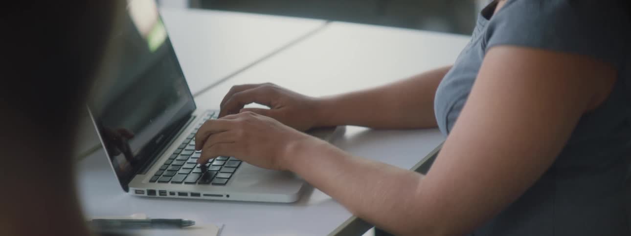 Woman sits at table typing on laptop