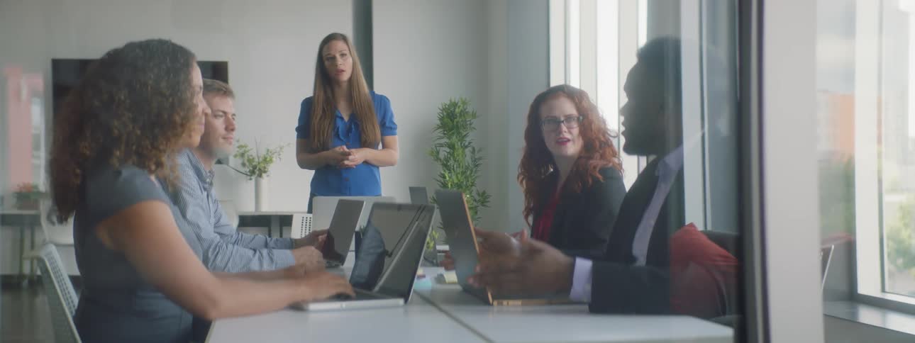 Team of coworkers sit at table with one woman standing
